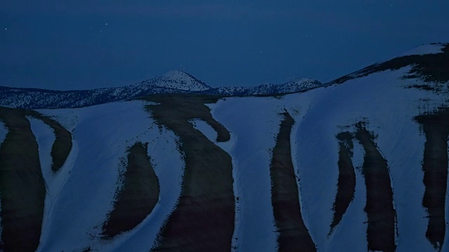 夜幕下的星星和白雪覆盖着冬日夜晚的彩绘山，在星星的照耀下视频素材