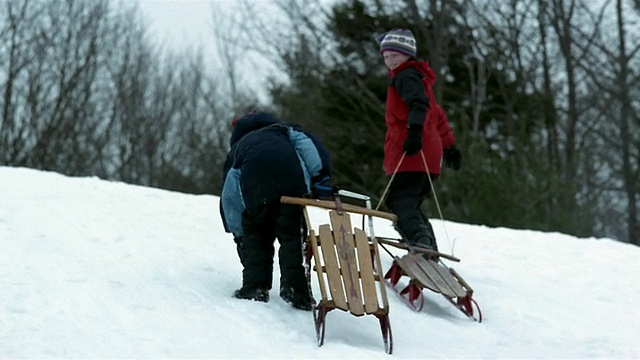 低角度中镜头男孩拖着雪橇爬上白雪覆盖的山丘视频素材