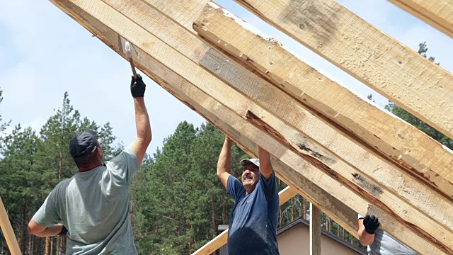 屋顶工人在屋顶上工作。建筑工人用锤子锤钉子。视频素材