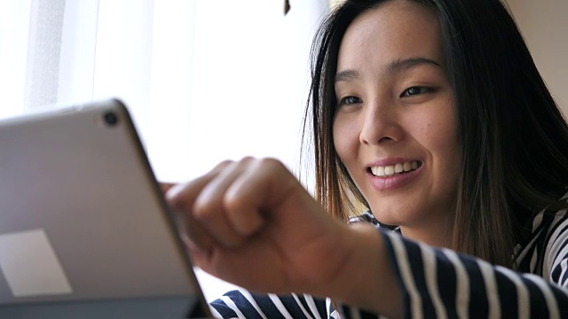 亚洲年轻女子在家里使用数字平板触屏电脑，慢镜头视频素材