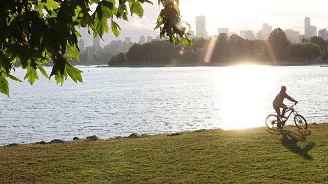 一名骑自行车的男子爬上沙滩上的草坡，后面是城市的天际线视频素材