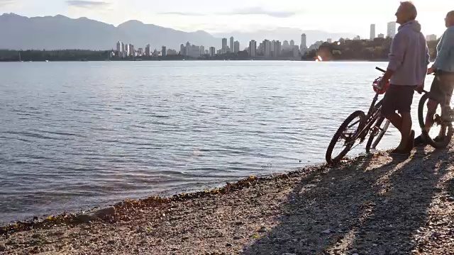 骑自行车的夫妇推着自行车穿过海滩，身后是城市的天际线视频下载