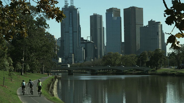 WS后视图的人骑在沿着河流的道路上，市中心天际线的背景，墨尔本，维多利亚，澳大利亚视频素材