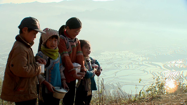 中国云南元阳，四个哈尼孩子拿着锅子，背景是稻田视频素材