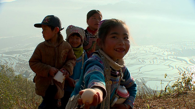 中国云南元阳，四个哈尼孩子拿着锅子，背景是稻田视频素材