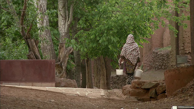 伊朗Abyaneh，一名妇女提着水桶走在乡村道路上视频素材