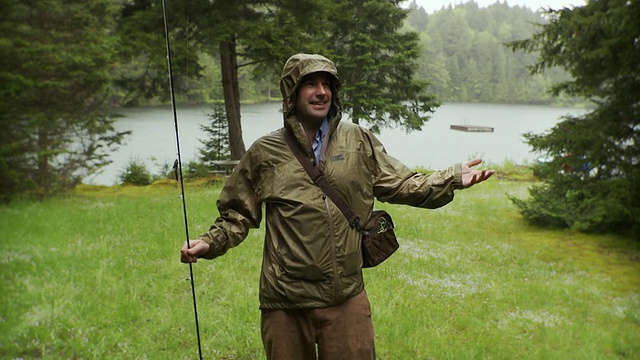 美国佛蒙特州莫里斯镇，一个微笑的男人拿着钓竿站在雨中，背景是湖视频素材