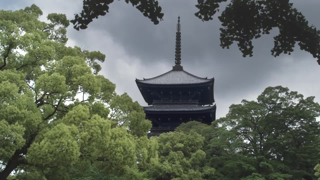 日本京都，多云的天空下，东寺五层宝塔顶部，前景中有树木视频素材