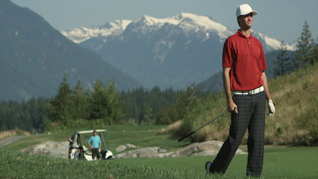 WS SLO MO男子挥动高尔夫球杆，年轻男子与高尔夫球车在背景/ Squamish，不列颠哥伦比亚省，加拿大。视频素材