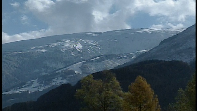 广角镜头在多云的天空下覆盖着雪山与松树林前景/瑞士视频素材