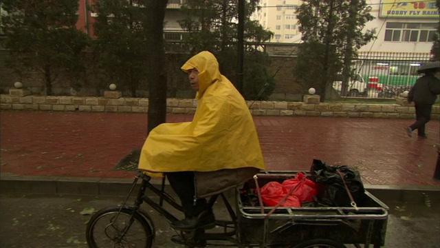 中国北京，一位老人穿着雨披骑着三轮自行车视频素材