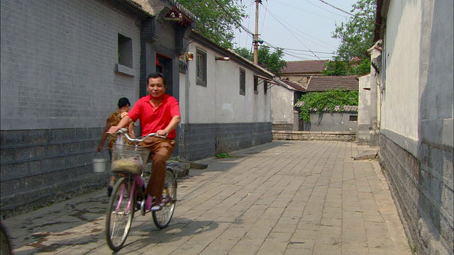 中国山东济南，两名男子骑着自行车穿过老城的小巷，一名女子扛着水罐视频素材