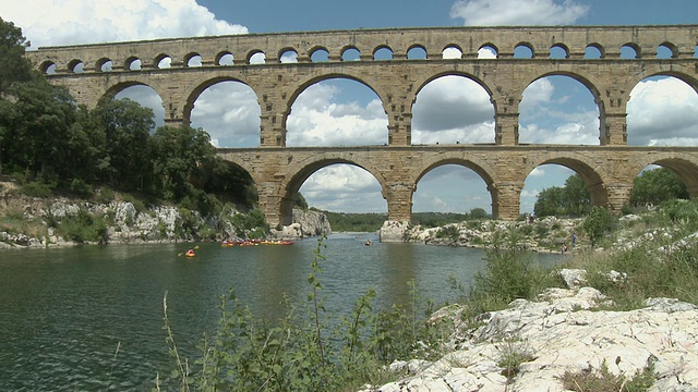 法国朗格多克-鲁西永，加德河的WS Pont du Gard，罗马高架渠，人们在远处的加德河上划独木舟视频素材