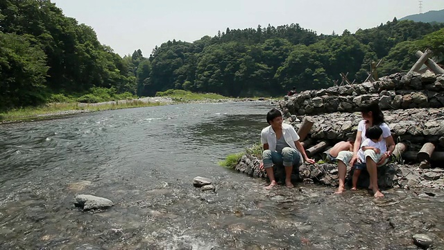 一对夫妇带着儿子(6-7岁)和女儿(2-3岁)坐在河边的岩石上/日本东京视频素材