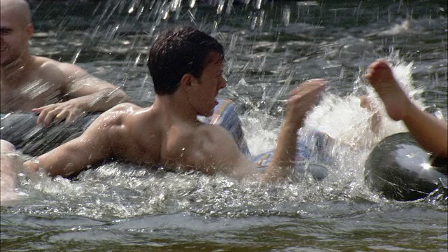 年轻男女漂浮在内胎上互相泼水/法明顿河，康涅狄格州视频素材