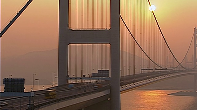 夕阳落在桥后，汽车在桥上行驶，太阳反射金色的光在下面的河流和朦胧的风景在B/G。MS朦胧的观点，金色的太阳在大桥后面的部分剪影。视频素材