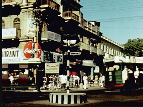 1960年蒙太奇街道标志:伊拉克沙阿和艾尔芬斯通圣卡拉奇街角，有轨电车穿过。位于巴基斯坦卡拉奇街头的大型白色建筑，带有泛美航空公司办公室视频素材