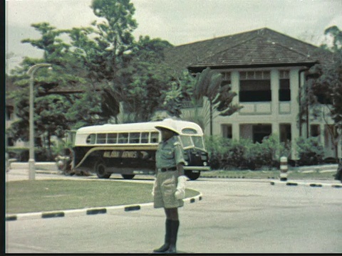 1957年，穿着短裤的警察用手势指挥交通。马来亚航空巴士驶过/新加坡/音频视频素材