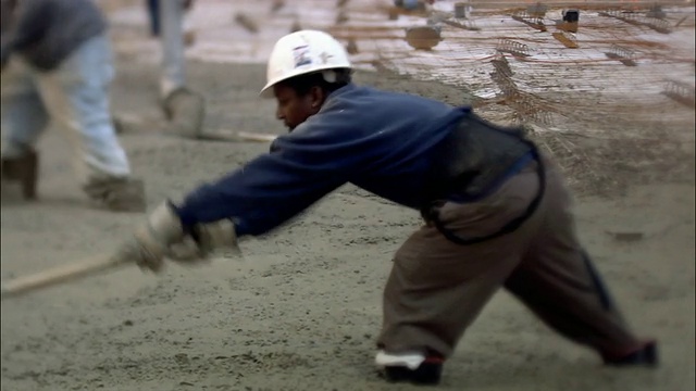 建筑工人站在湿漉漉的水泥地上，用铁锹把它铲平/在水泥地上倾斜腿/纽约市视频素材