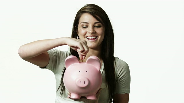 MS Portrait of young woman holding pig储蓄罐against white background / Orem, Utah, USA视频素材