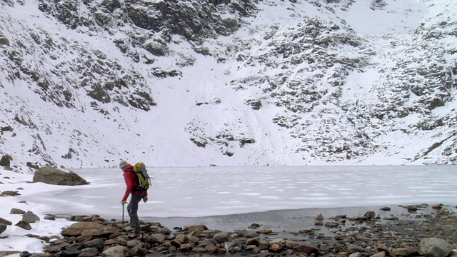 登山者走在冰冻的山湖，背景是白雪覆盖的山/ Llanberis，斯诺登尼亚，英国视频素材