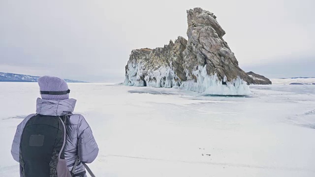 女人在贝加尔湖冰面上的旅行。冬岛之旅。女孩在冰岩石下行走。游客看着美丽的冰洞。极限跋涉和步行。背包客在大自然中休憩。视频素材