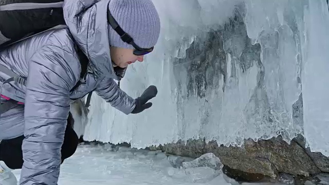 女人在贝加尔湖冰面上的旅行。冬岛之旅。女孩在冰岩石下行走。游客看着美丽的冰洞。极限跋涉和步行。背包客在大自然中休憩。视频素材