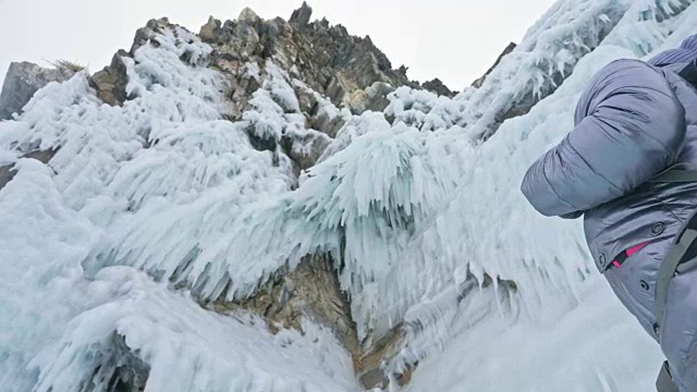 女人在贝加尔湖冰面上的旅行。冬岛之旅。女孩在冰岩石下行走。游客看着美丽的冰洞。极限跋涉和步行。背包客在大自然中休憩。视频素材