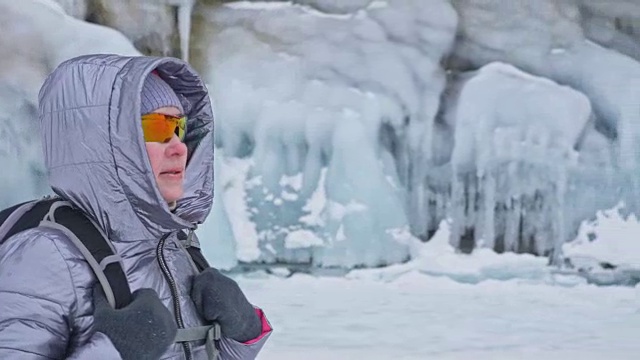 女人在贝加尔湖冰面上的旅行。冬岛之旅。女孩在冰岩石下行走。游客看着美丽的冰洞。极限跋涉和步行。背包客在大自然中休憩。视频素材