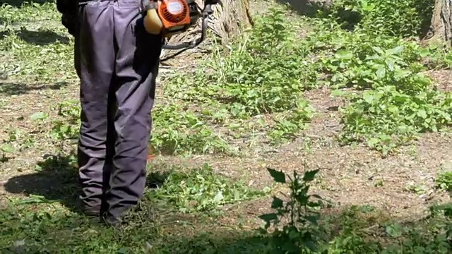 在慢镜头中，一名男子用便携式割草机割草视频素材