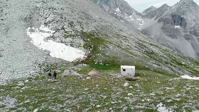 航拍:飞过一对正在山上小屋附近散步的徒步旅行者。视频素材