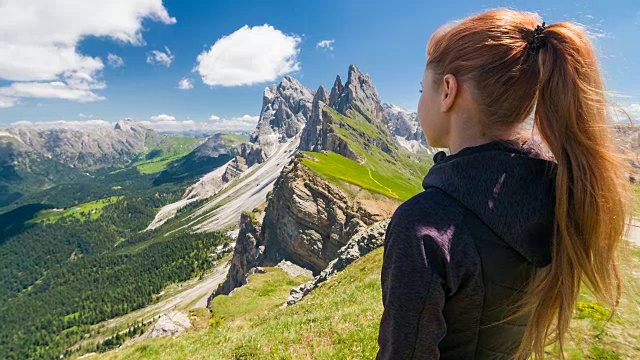 女游客探索山坡，站在山顶，欣赏周围的壮丽的山在一个美丽的阳光灿烂的日子视频素材