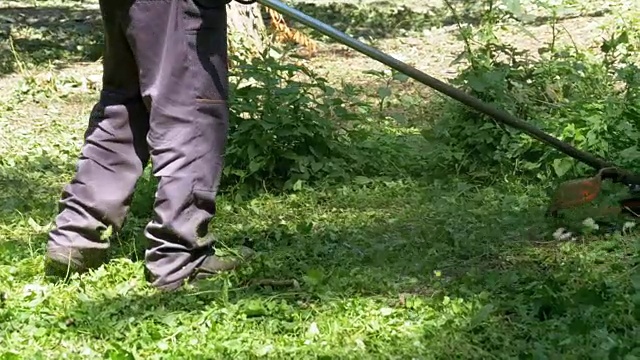 在慢镜头中，一名男子用便携式割草机割草视频素材