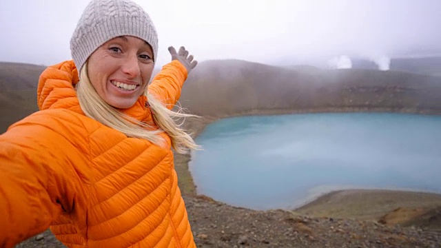 一名身穿橙色雨衣的年轻女子在冰岛与火山景观自拍。人旅游探险理念视频素材