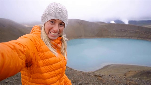 慢动作——一名身穿橙色雨衣的年轻女子与冰岛的火山景观自拍。人旅游探险理念视频素材