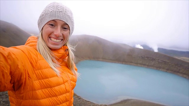 慢动作——一名身穿橙色雨衣的年轻女子与冰岛的火山景观自拍。人旅游探险理念视频素材