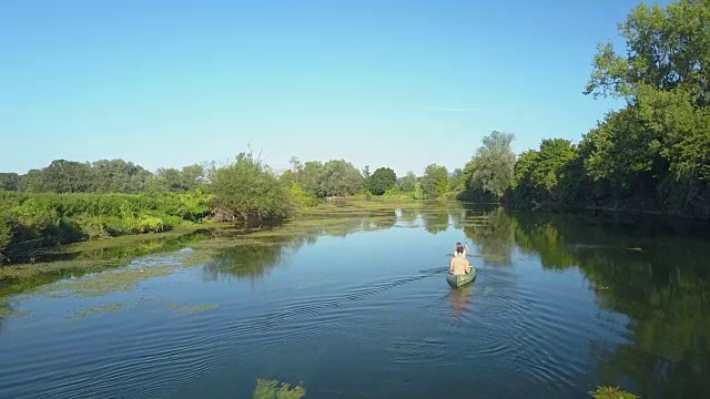 天线:活跃的年轻夫妇划着他们的独木舟沿着一条宁静的深蓝色河流而下。视频素材