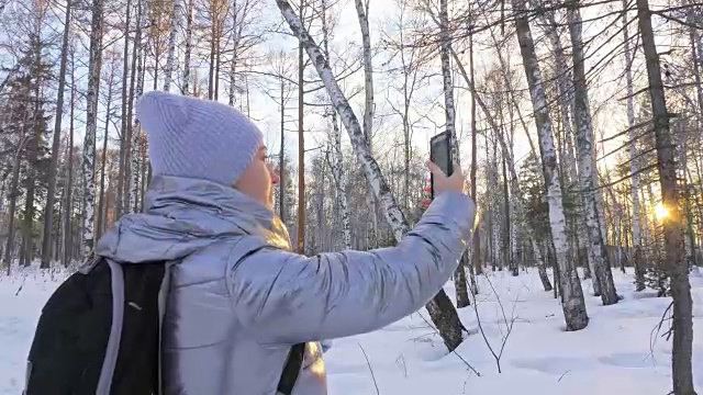 一个女人走在树林里。旅行者在森林里用手机拍照。女孩会自拍，用智能手机交流。美丽多汁的日落时分。视频素材