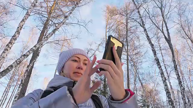 一个女人走在树林里。旅行者在森林里用手机拍照。女孩会自拍，用智能手机交流。美丽多汁的日落时分。视频素材