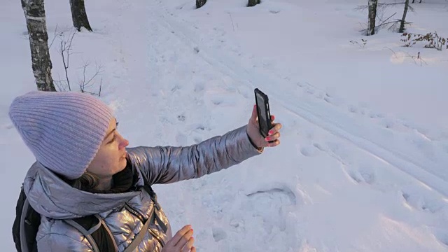 一个女人走在树林里。旅行者在森林里用手机拍照。女孩会自拍，用智能手机交流。美丽多汁的日落时分。视频素材