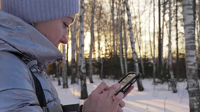 一个女人走在树林里。旅行者在森林里用手机拍照。女孩会自拍，用智能手机交流。美丽多汁的日落时分。视频素材