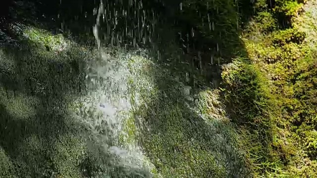 慢镜头，瀑布在山上高速卷。特写的春天的水滴下落和溅在绿色的苔藓视频素材