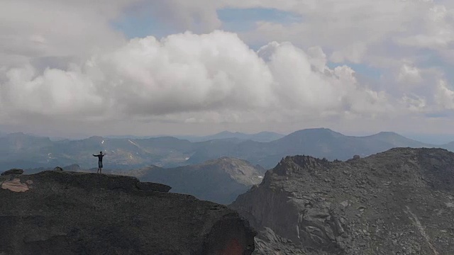 一个男人站在山顶的航拍照片。年轻的登山者爬完山高兴地举起了手。视频素材