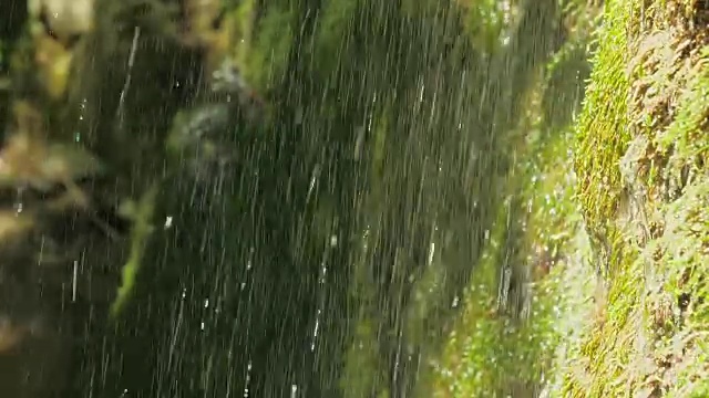 慢镜头，瀑布在山上高速卷。特写的春天的水滴下落和溅在绿色的苔藓视频素材