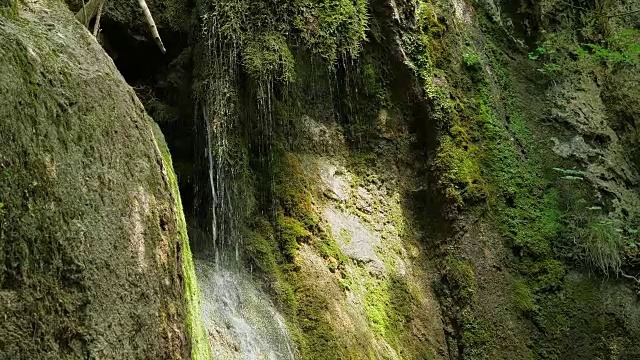 慢镜头，瀑布在山上高速卷。特写的春天的水滴下落和溅在绿色的苔藓视频素材