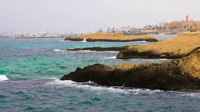 在蓝色的天空和地平线背景上，海浪拍打着岩石岛视频素材