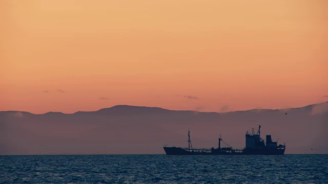 一艘巨大的货船在夕阳的黄色光芒中漂浮在海上视频素材