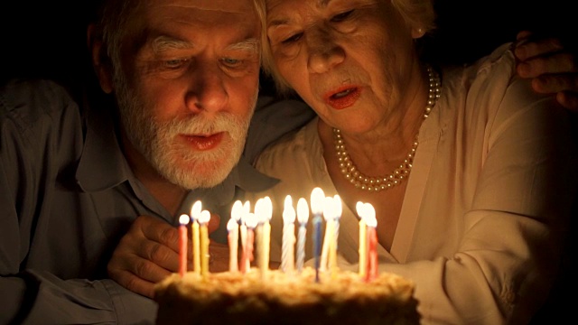 相爱的老年夫妇晚上在家用蛋糕庆祝结婚纪念日。吹灭蜡烛视频素材