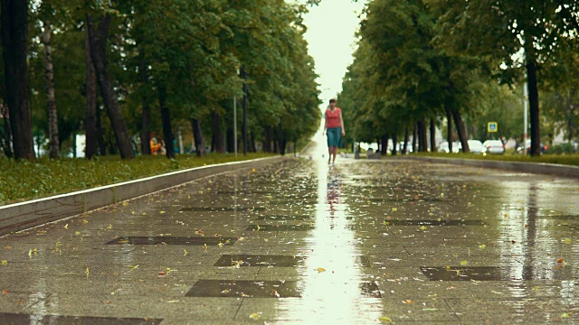 下雨的时候，一个穿着蓝凉鞋的年轻女子走在公园的湿路上。视频素材