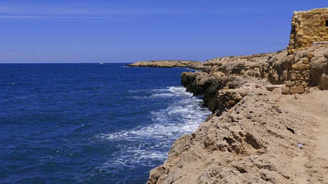 海浪拍打着岩石海岸，在地平线上有堡垒的背景视频素材